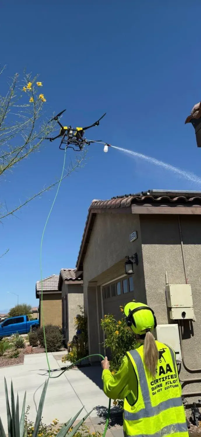 DronePower1 drone spraying a home while an operator manages the hose below in the courtyard