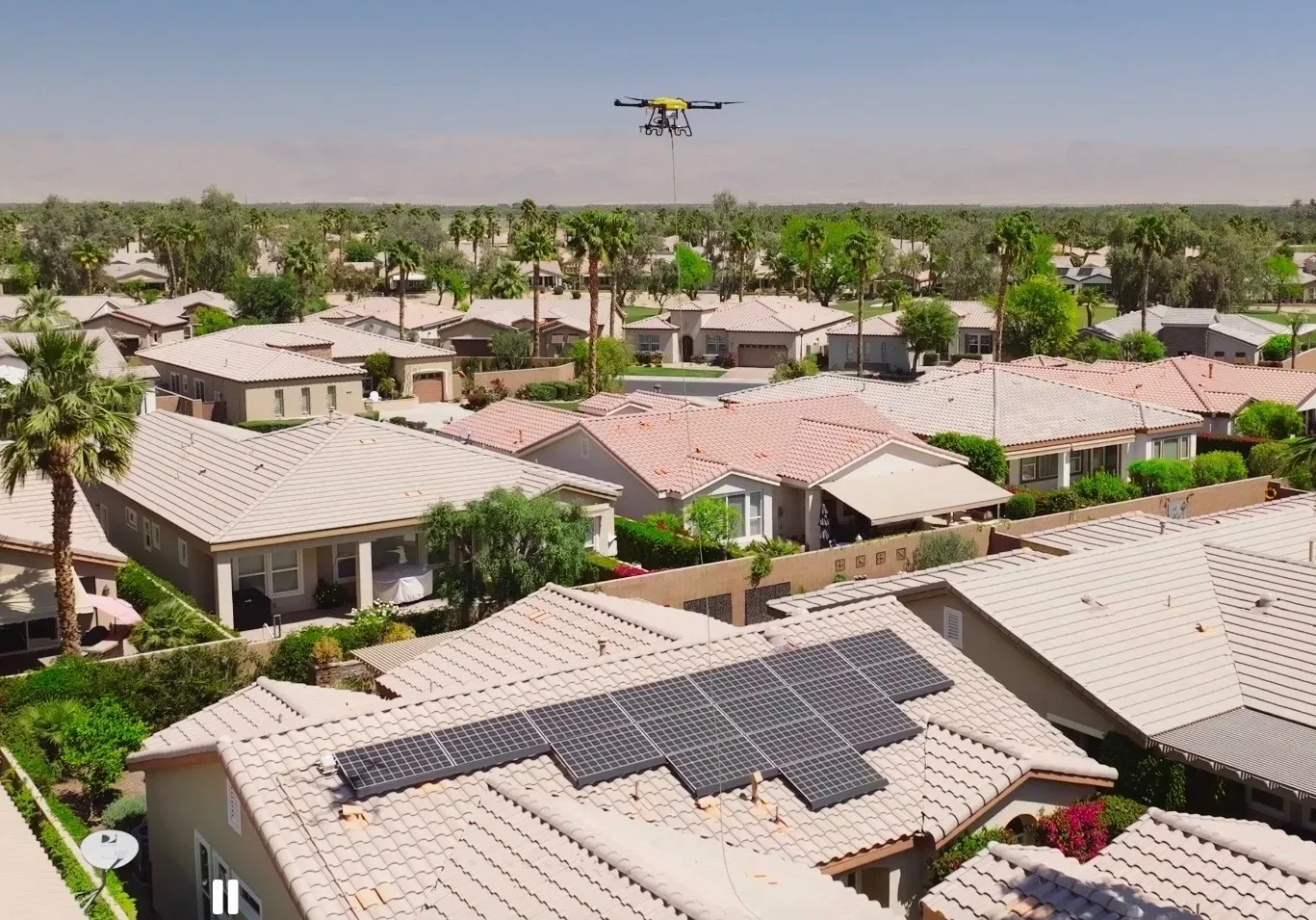 Wide aerial view of neighborhood rooftops with a DronePower1 drone over a solar array