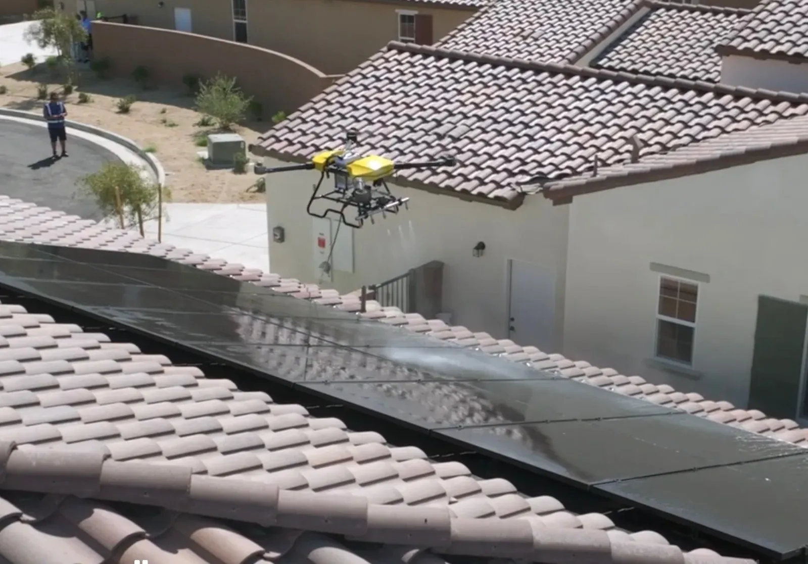 DronePower1 drone making a cleaning pass over a roof with the operator managing the hose below