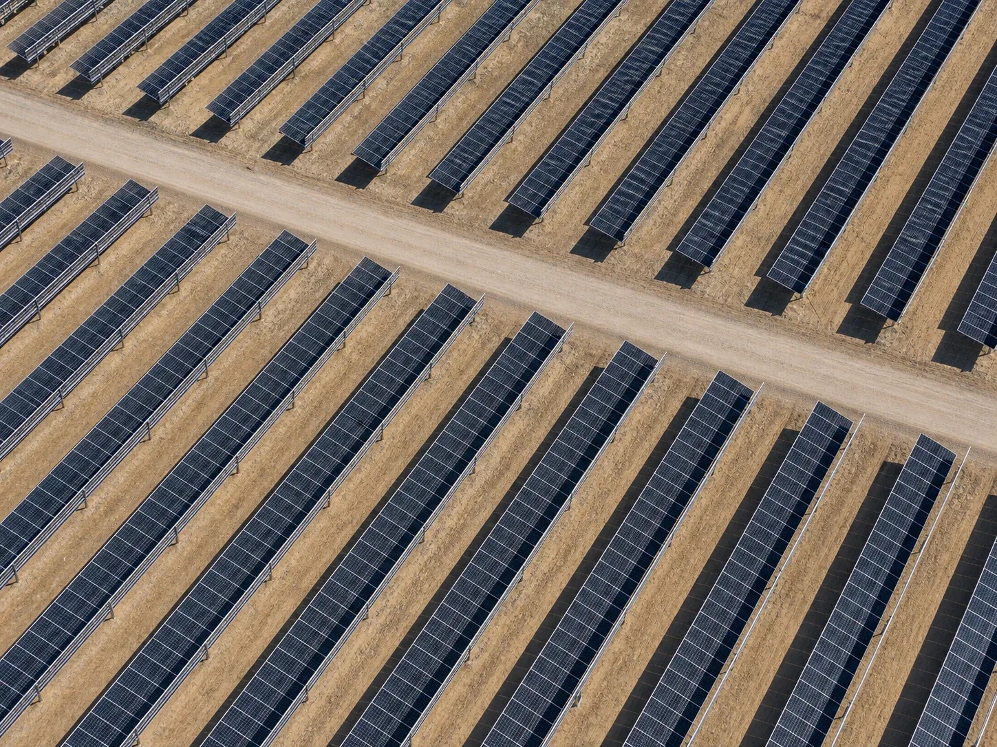 Top-down aerial view of repeating ground-mounted solar rows and a gravel cross-access lane